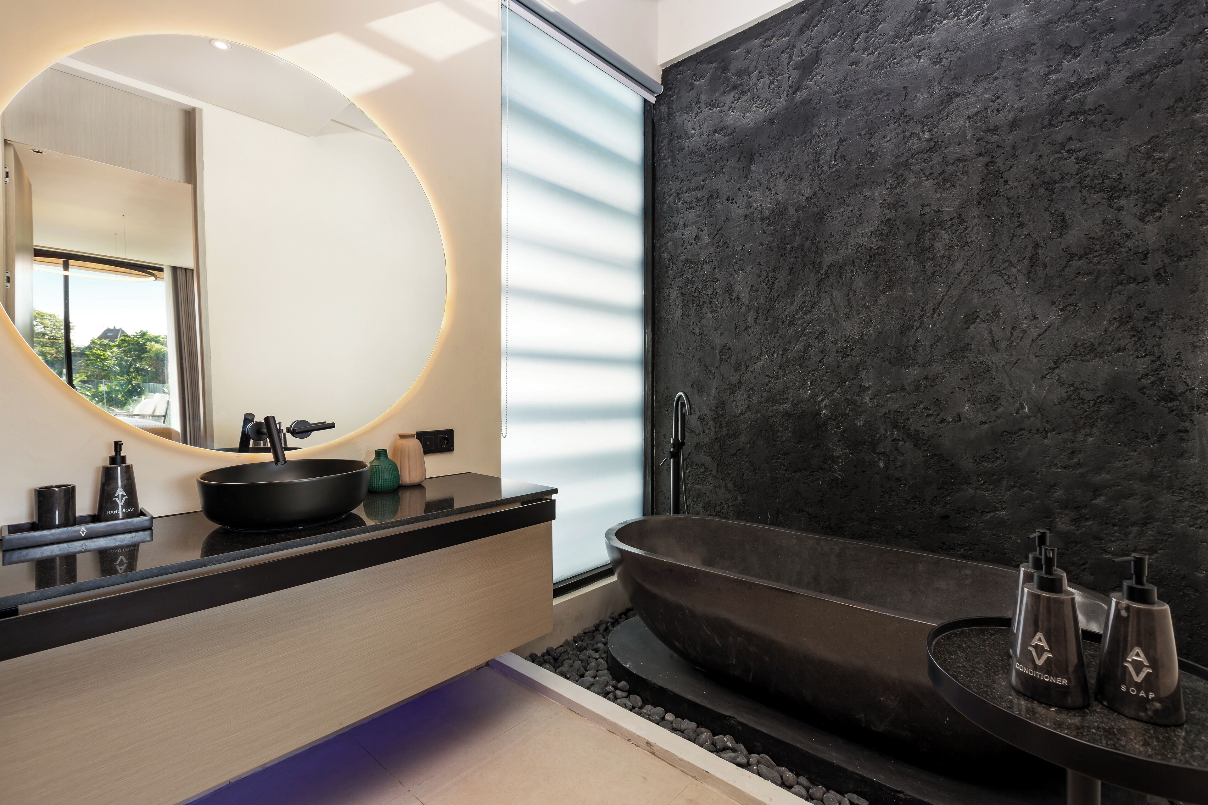 Une salle de bain moderne avec un grand miroir rond, une baignoire noire et un meuble-lavabo élégant doté d’un plan de toilette noir.