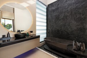 Un baño moderno con un espejo redondo grande, una bañera negra y un mueble de tocador elegante con encimera negra.