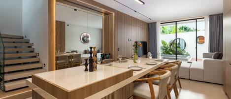 Une cuisine moderne dotée d’un îlot central, de meubles en bois et d’un coin repas avec une longue table et des chaises.