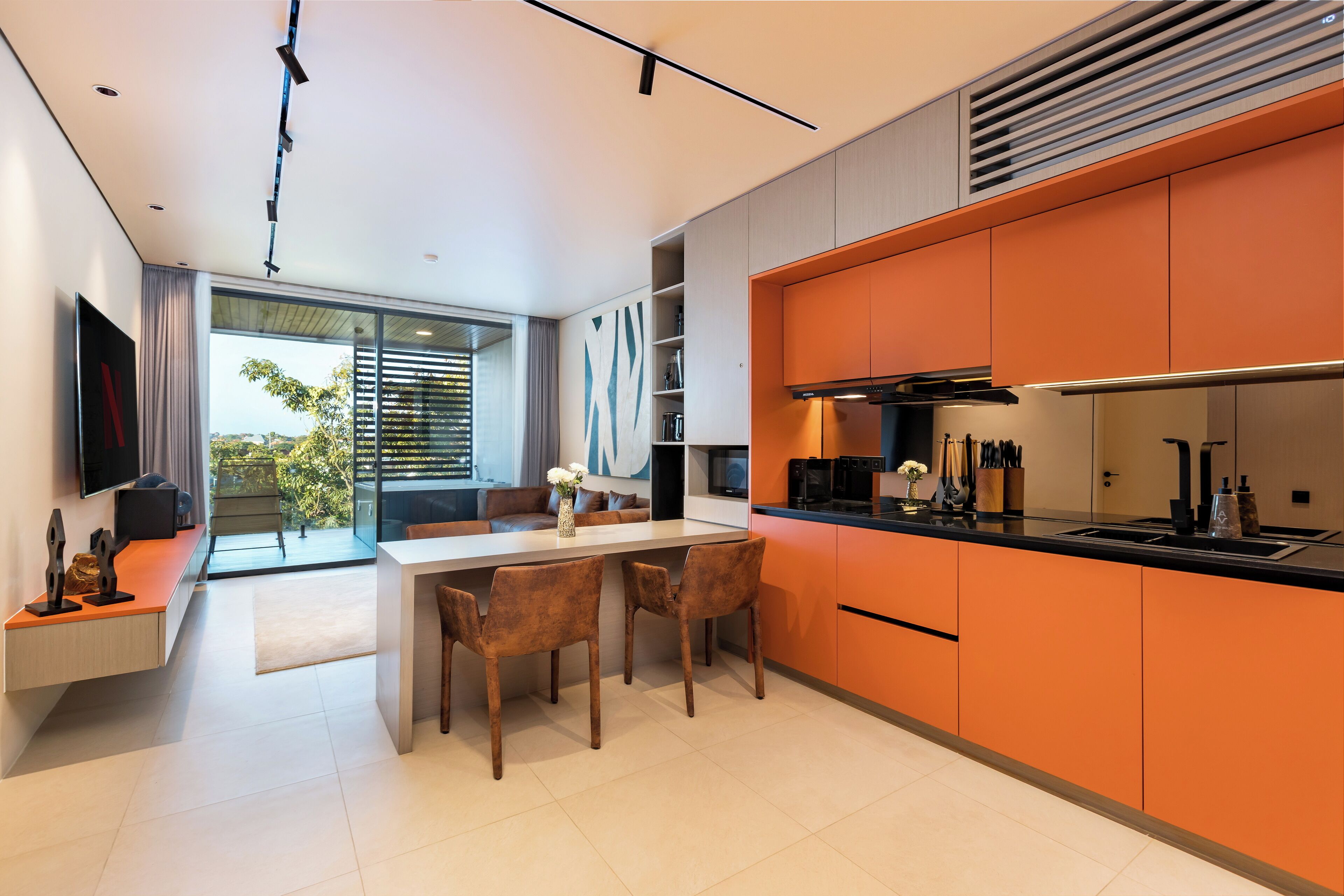 A modern kitchen with orange cabinets, a black countertop, and a dining area with two chairs and a table.