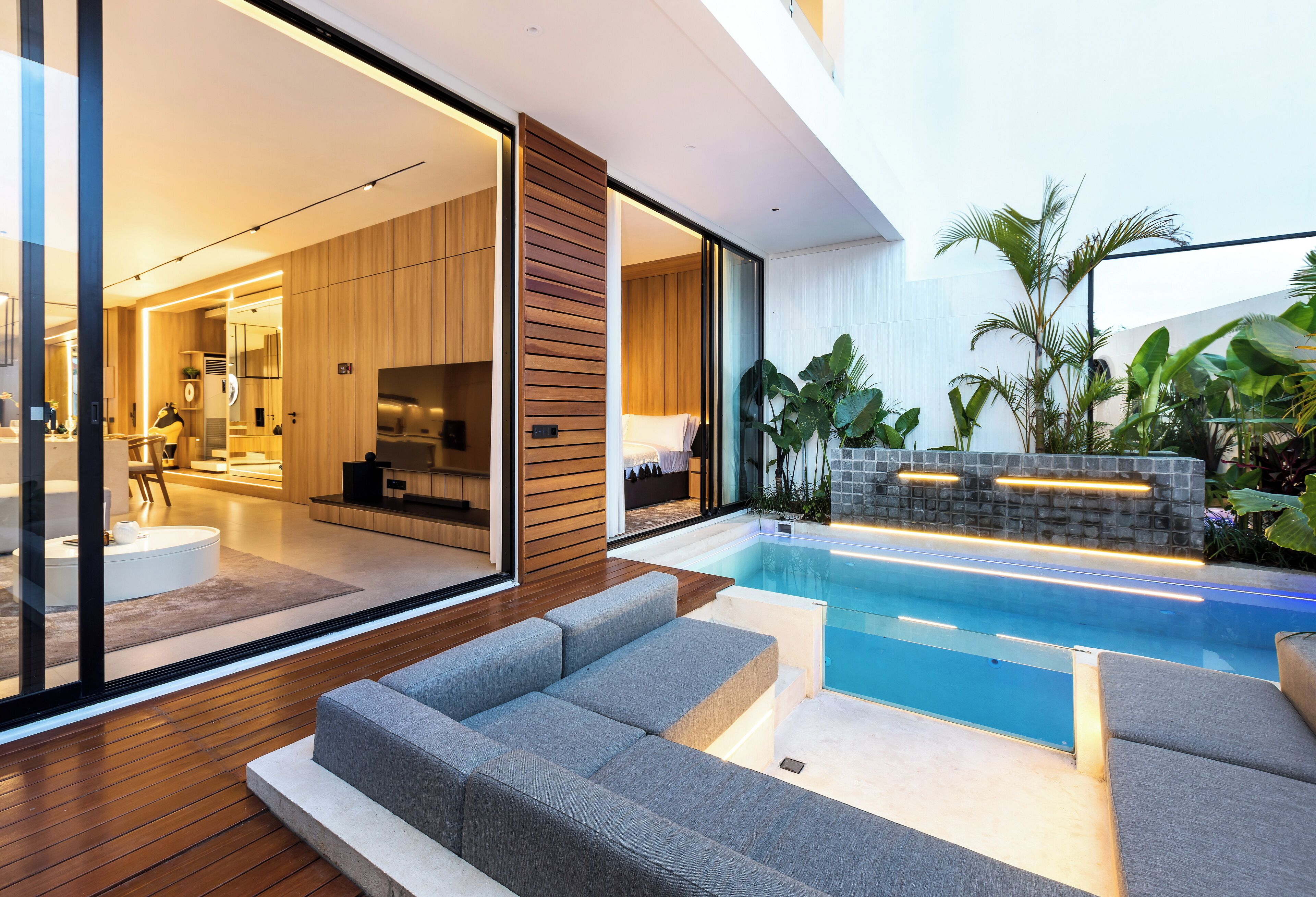 A modern living area with a pool, wooden flooring, and a glass door leading to a kitchen.