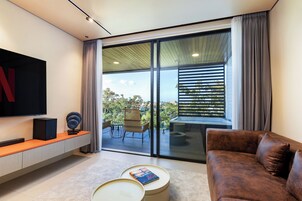 Un salon moderne doté d’un grand téléviseur, d’un canapé en cuir marron, d’une table basse et d’une porte-fenêtre coulissante donnant sur un balcon extérieur.