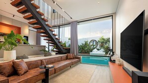 A modern living room with a large TV, a sofa, a staircase, and a pool view. - Alex Villas Complex N5 (Canggu)