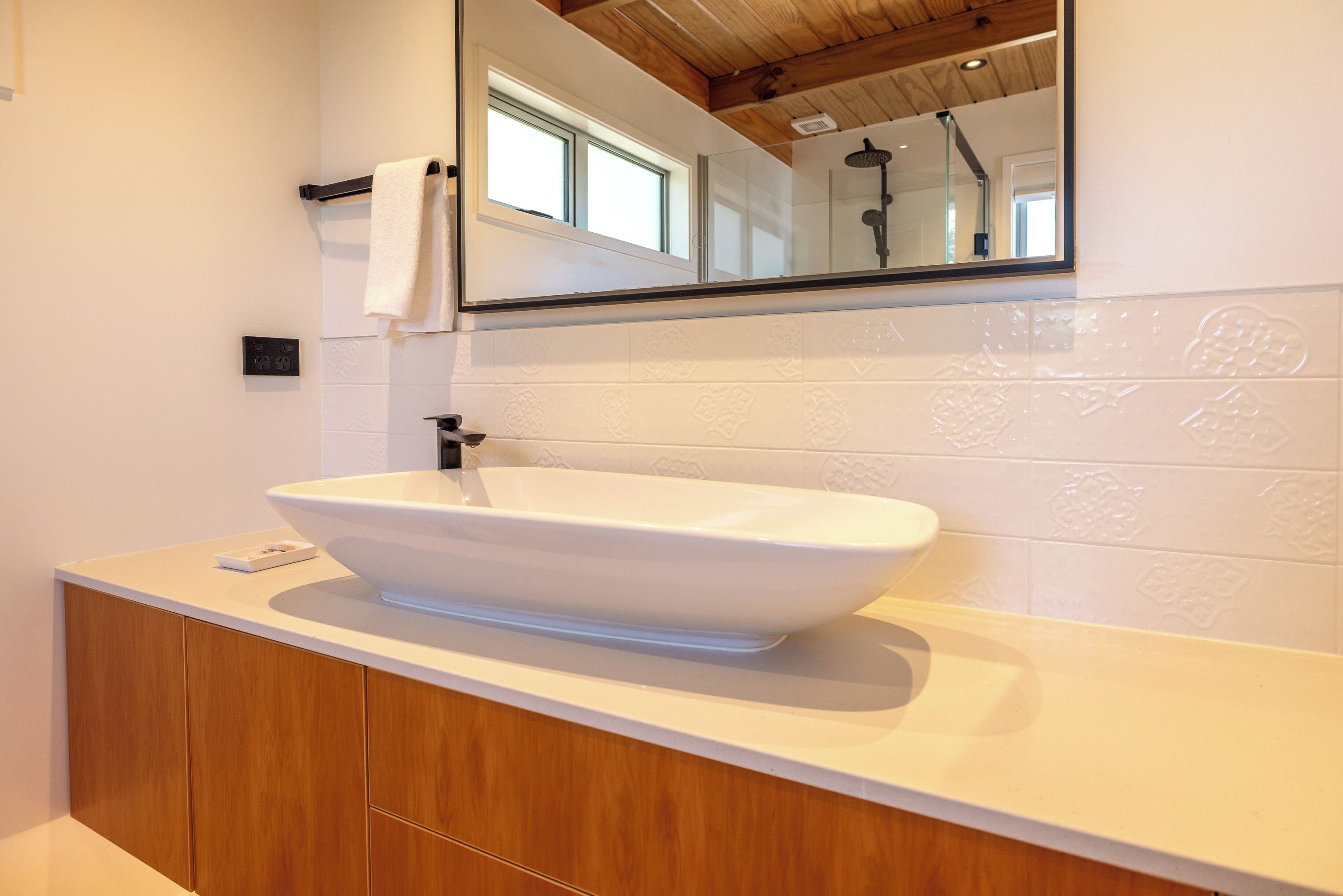 Une salle de bain avec un lavabo sur colonne blanc, des meubles en bois, un miroir et une fenêtre.