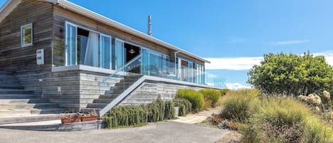 A modern house with a wooden exterior, large glass windows, and a staircase leading to a balcony.
