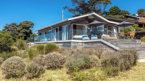 Una casa moderna con fachada de vidrio, terraza de madera y zona de estar al aire libre.