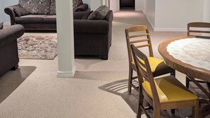 A spacious living room with a dark grey sofa, a smaller grey sofa, and a round wooden table with yellow chairs. A patterned rug is on the floor. - Grapeview Lower Level Apartment (St. Catharines)