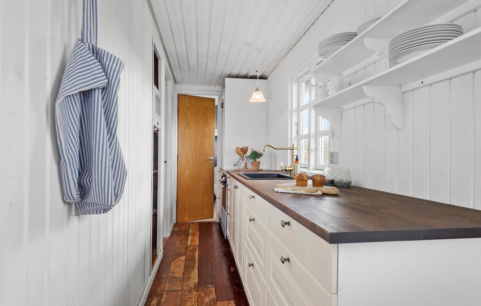 Een smalle keuken met witte kastjes, een houten aanrechtblad en een gestreepte handdoek.