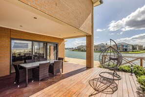 Um deck de madeira com mesa e cadeiras, uma cadeira suspensa e vista para casas sobre a água.