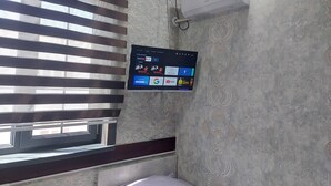 A room with a mounted air conditioner, a window with blinds, and a wall-mounted digital screen displaying various apps. - Sokin (Bukhara)