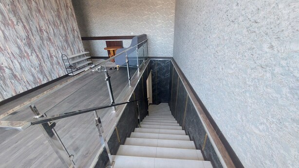 A staircase with a marble wall on one side and a wooden floor on the other, leading to a landing with a chair and a small table. - Sokin (Bukhara)