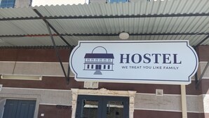 A hostel sign with a house icon and the text "HOSTEL WE TREAT YOU LIKE FAMILY". - Sokin (Bukhara)
