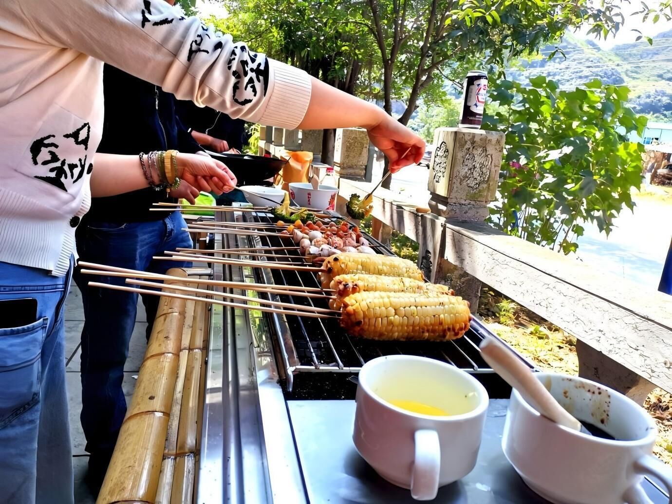 A person grilling food outdoors with a table containing a mug and a bowl.