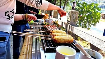A person grilling food outdoors with a table containing a mug and a bowl.
