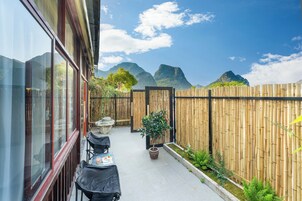 Un patio con mesas y sillas, una cerca de bambú y vistas a montañas.