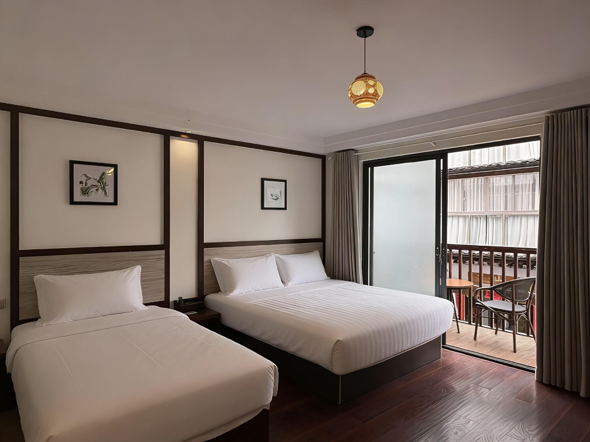 Een hotelkamer met twee bedden, een balkon met een tafel en stoelen, en een groot raam.