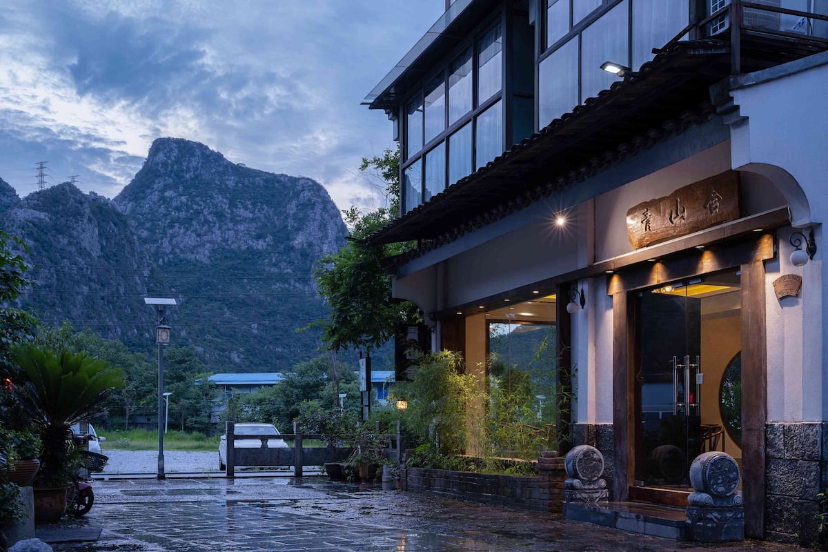 A hotel with a traditional architectural style, a mountain backdrop, and a well-lit entrance.