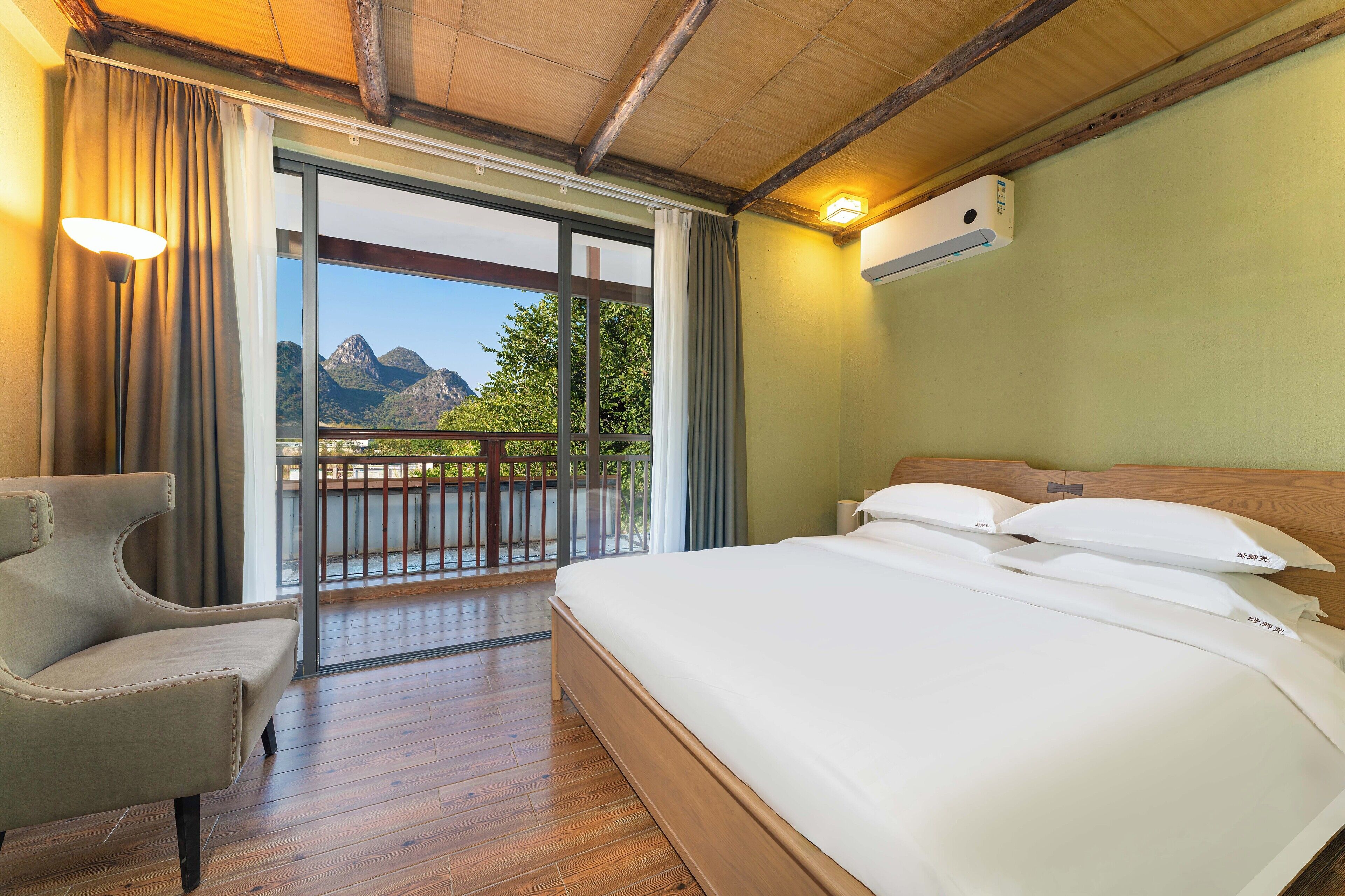 Een hotelkamer met een bed, een stoel, een balkon met uitzicht op bergen, en een airconditioning.