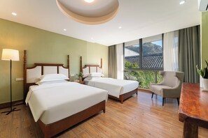 A hotel room with two beds, a chair, a table, and a large window with a view of a traditional roofed building. - Serene Vale Inn Guilin (Guilin)