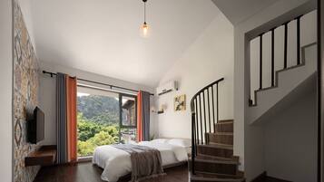 A bedroom with a bed, a TV, a window with curtains, a staircase, and a view of greenery.