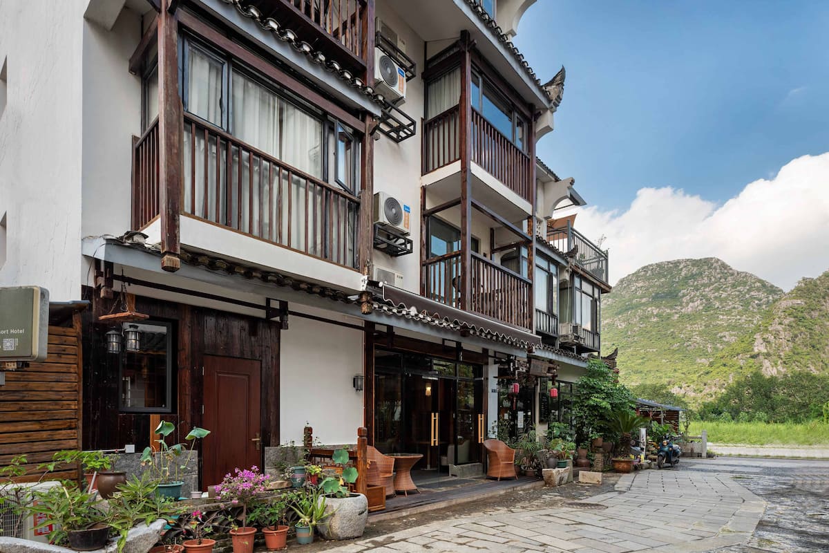 A multi-story building with balconies, potted plants, and a mountainous backdrop.