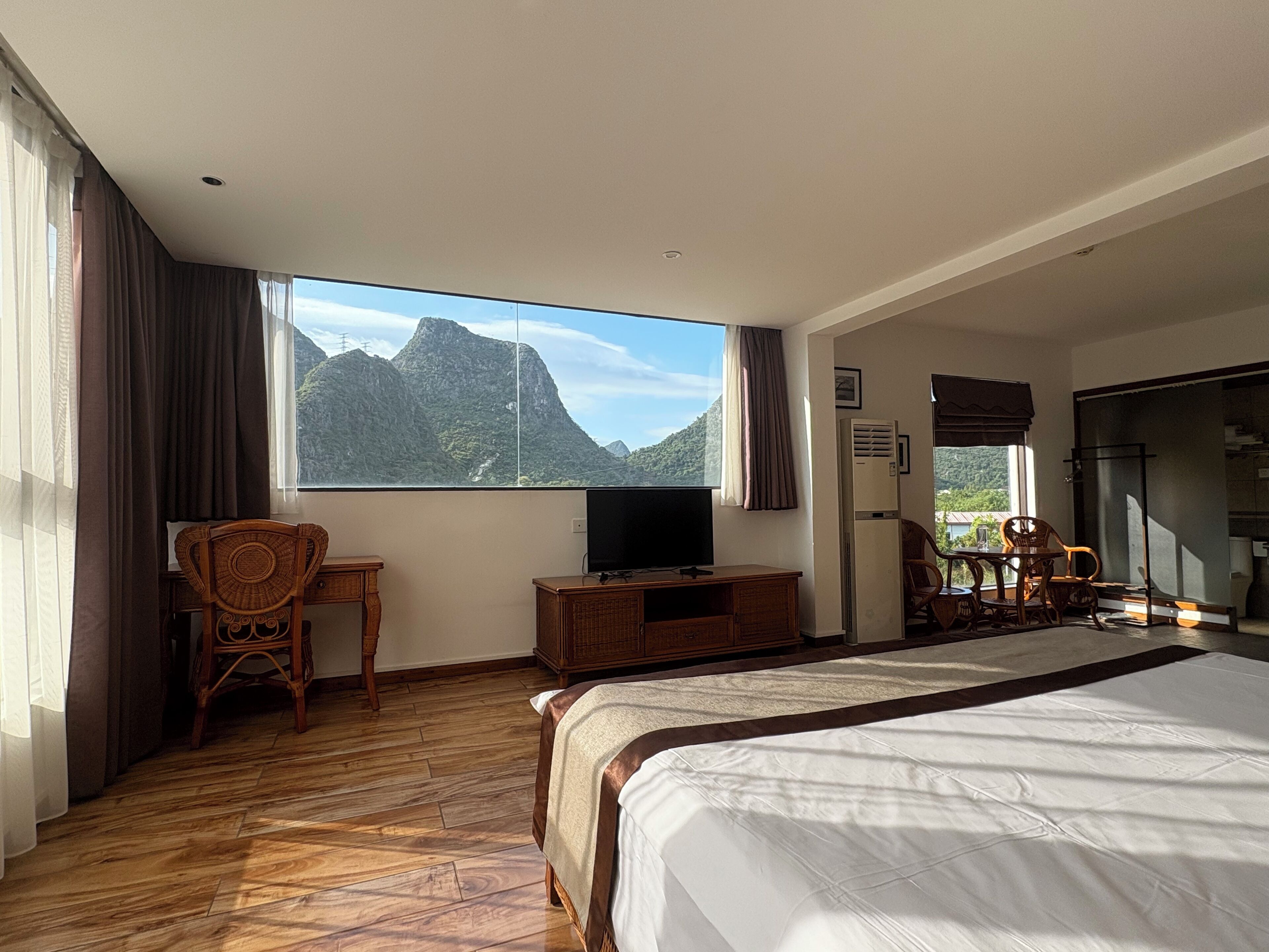 A hotel room with a bed, a TV, a desk, and a view of mountains.