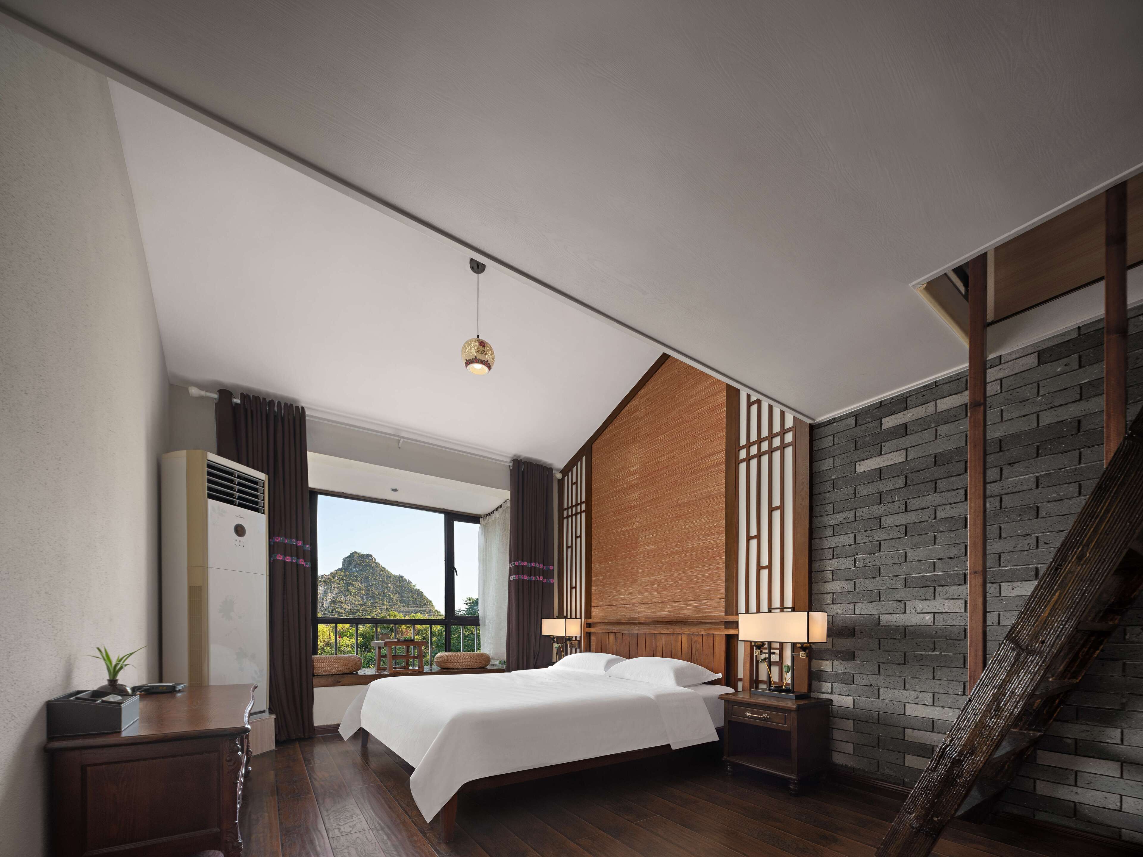 A modern hotel room with a large bed, a desk, a nightstand, a lamp, and a view of the outdoors.