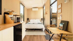 Habitación de hotel compacta con cama, kitchenette, mesa de comedor y un amplio ventanal.