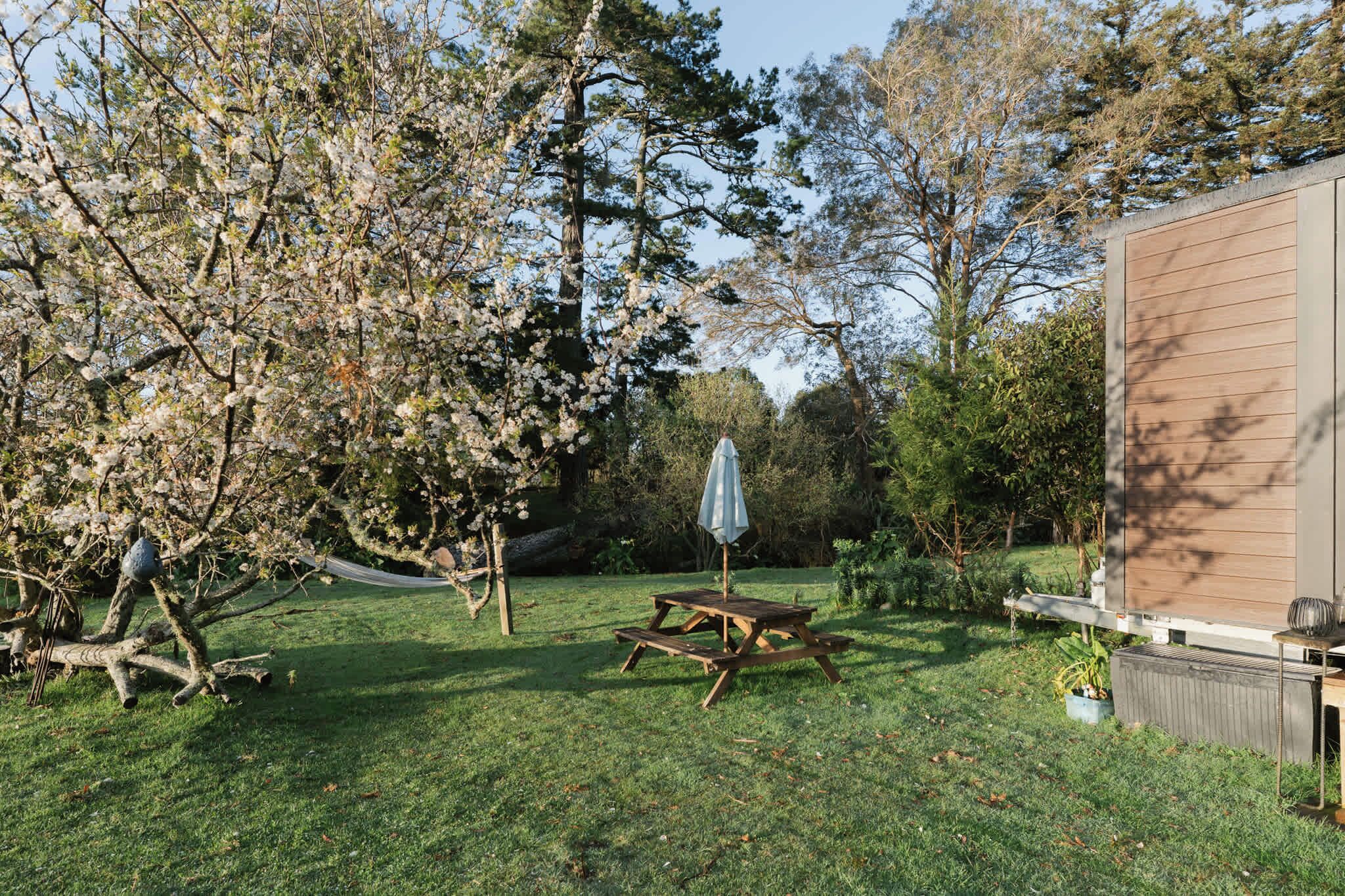 Een achtertuin met een houten picknicktafel, een hangmat en een klein parasol.