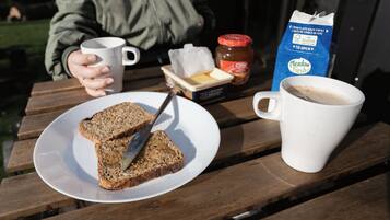 Une table en bois sur laquelle se trouvent une assiette de toasts, un pot de confiture, un paquet de beurre, une tasse de café et un carton de lait.