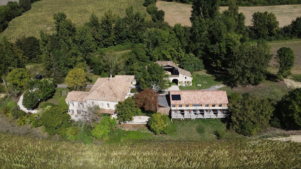 An aerial view of a property with a large house, a barn, and surrounding greenery.