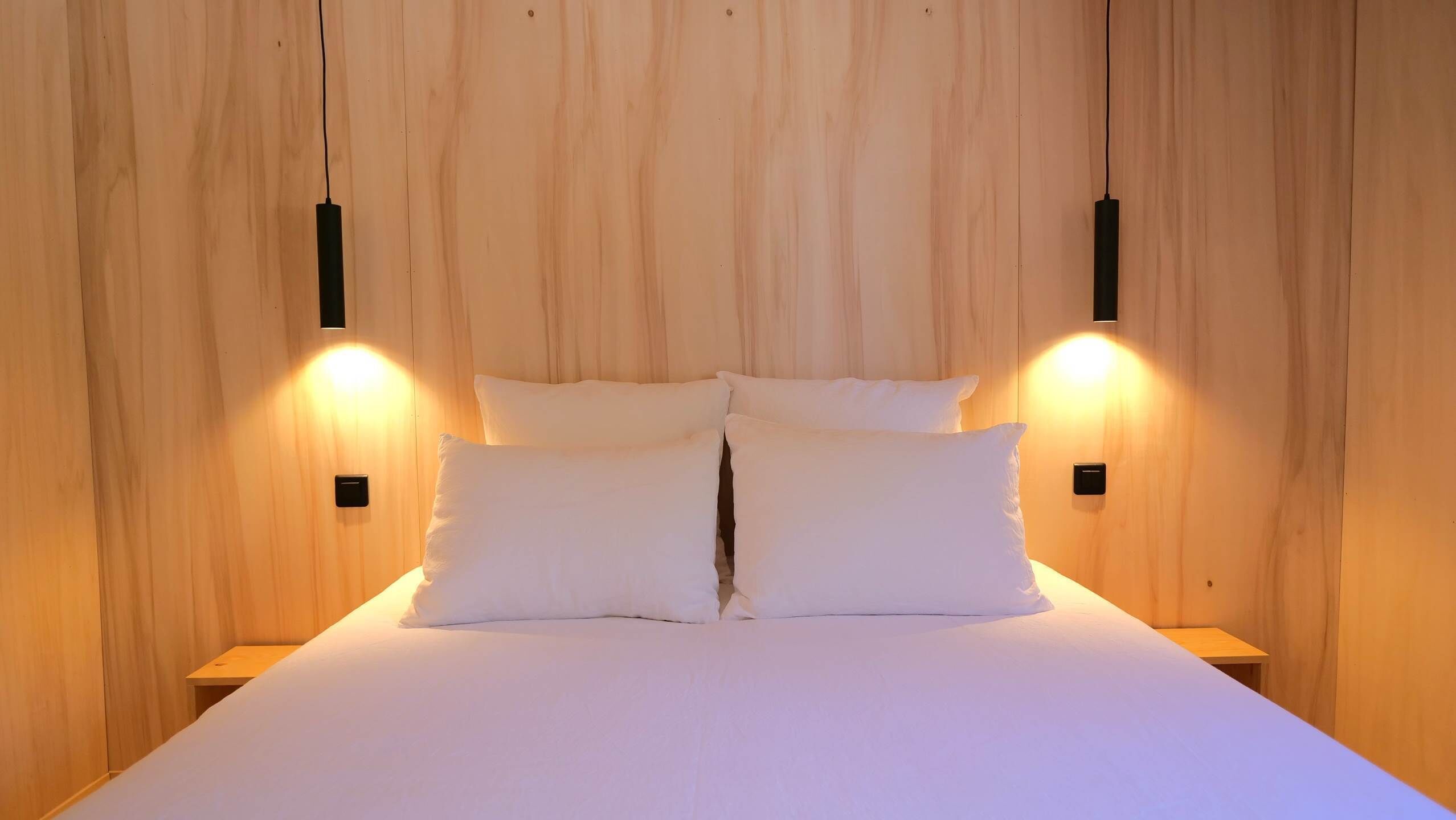 Un lit avec du linge de lit blanc et deux tables de chevet, chacune dotée d’un interrupteur noir.