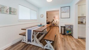 Una cucina con tavolo in legno, mobili bianchi e una finestra con persiane.