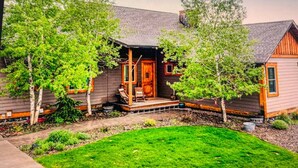 Ein Holzhaus mit Veranda, umgeben von Bäumen und einem gepflegten Rasen.