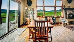 Ein Essbereich mit einem Holztisch und -stühlen, einem Kamin und Blick auf eine grüne Landschaft durch große Fenster.