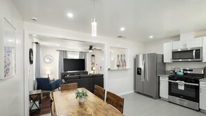 A modern kitchen with stainless steel appliances, a dining area with a wooden table, and a living room with a sofa and TV. - Upgraded 2Bed/1B on Quiet Street w. Easy Access  to US99 (Fresno)