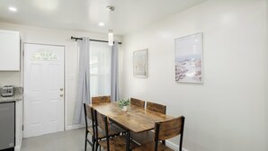 A dining area with a wooden table and chairs, a white door, a kitchen area, and two framed pictures on the wall. - Upgraded 2Bed/1B on Quiet Street w. Easy Access  to US99 (Fresno)