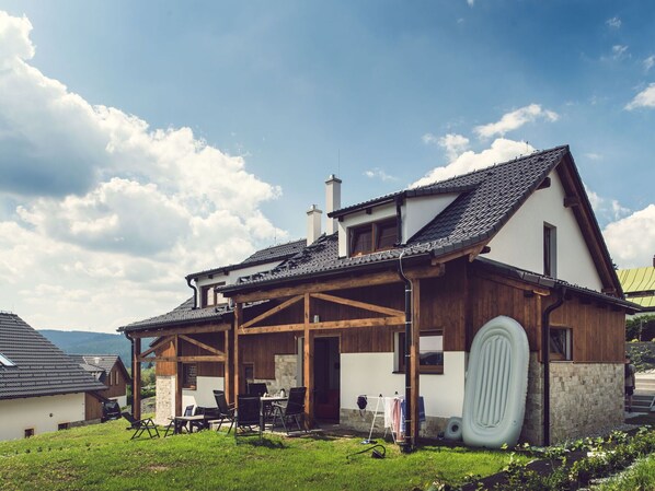 Una casa de dos pisos con un porche de madera, una chimenea y una pared exterior blanca.