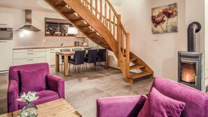Une cuisine moderne avec un escalier en bois, un coin repas avec des meubles violets et un poêle à bois.