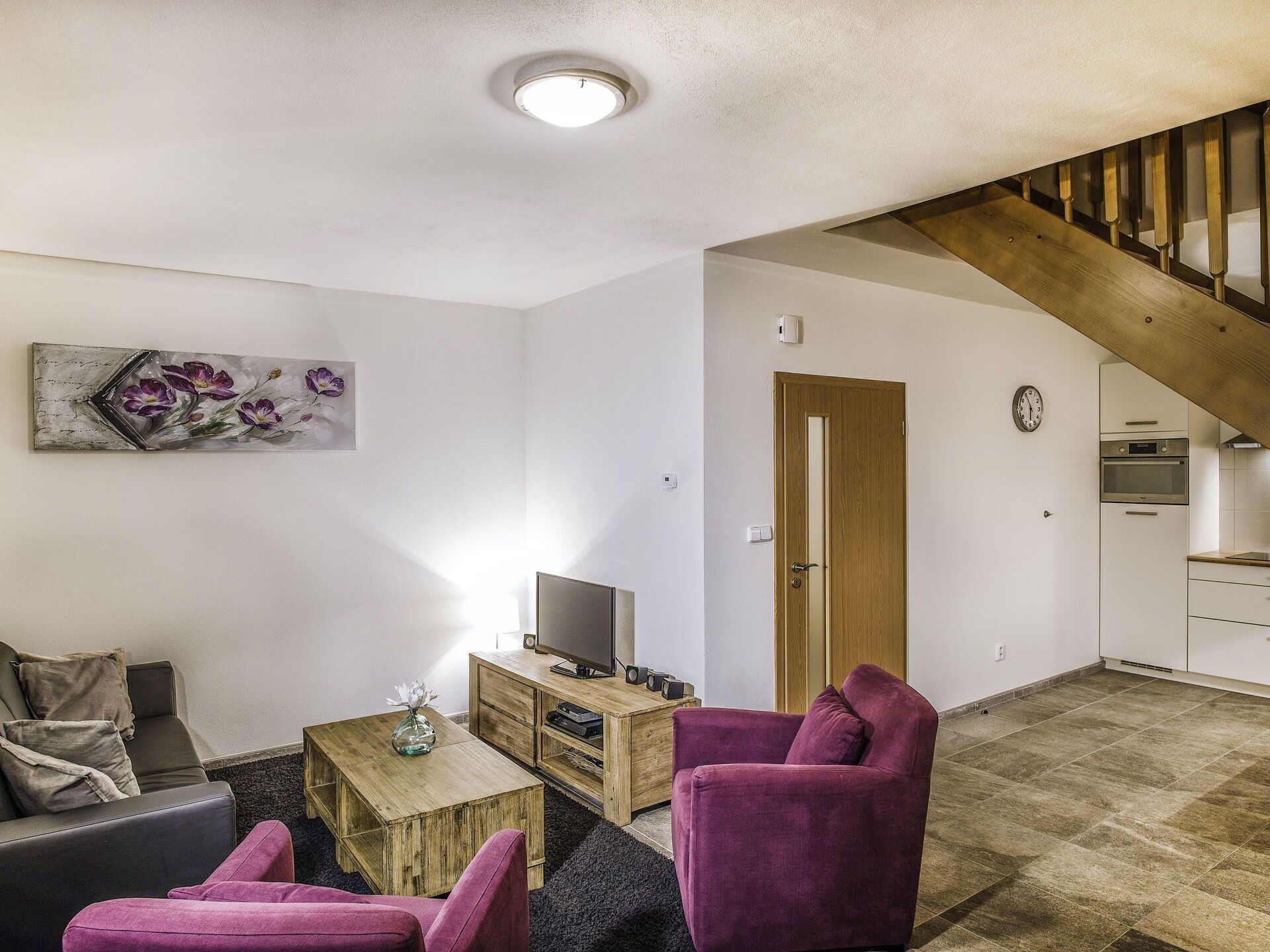 Ein Wohnzimmer mit einer Couch, einem Couchtisch, einem Fernseher und einer Treppe, die in eine Küche führt.