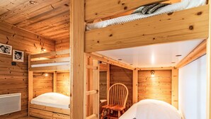 Una habitación de cabaña de madera con literas, una silla y una pequeña mesa.
