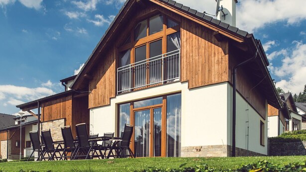 Ein zweistöckiges Haus mit Holzfassade, großen Fenstern und einem Balkon mit Sitzgelegenheiten.