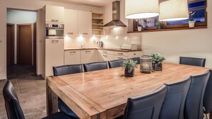 Eine moderne Küche mit Essbereich, ausgestattet mit einem Holztisch, schwarzen Stühlen, Pendelleuchten und einem Einbauofen.