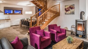 Ein modernes Wohnzimmer mit einer Holztreppe, einem Kamin und einem Essbereich, im Hintergrund ist eine Küche zu sehen.