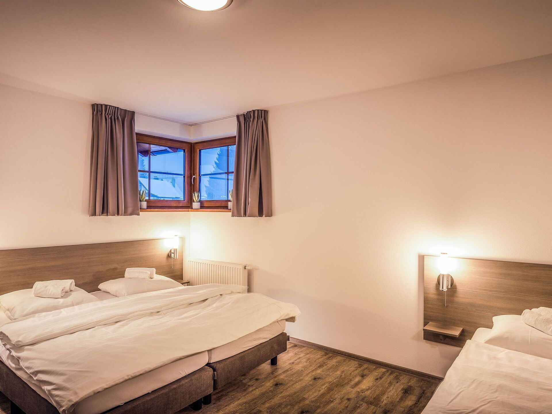 A hotel room with a large bed, two bedside tables, a window with curtains, and a wall-mounted light fixture.