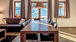 Un salon moderne avec une table à manger en bois, un canapé en cuir et de grandes fenêtres dotées de rideaux.