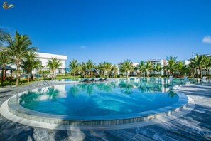 A large, circular infinity pool with clear blue water, surrounded by palm trees and modern buildings. - Golden Sea Resort (Cửa Việt)