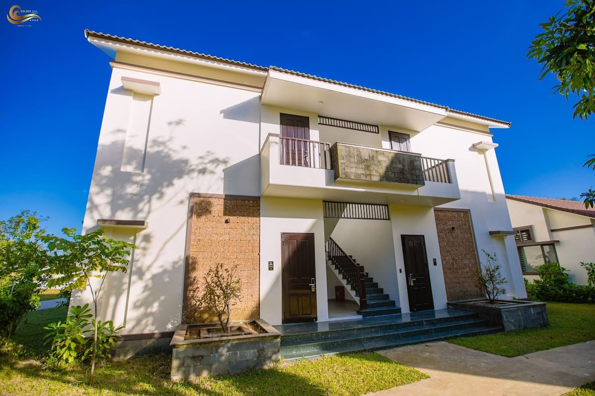 A two-story building with a balcony, a staircase, and a small garden area.