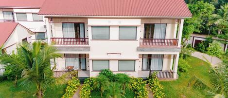 A multi-story hotel with a red roof, balconies, and a garden with yellow flowers.