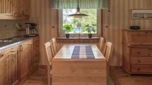 Ein Holzespeisesaal mit sechs Stühlen, ein Fenster mit Pflanzen und eine Küchenzeile mit Holzschränken und einer Kaffeemaschine.